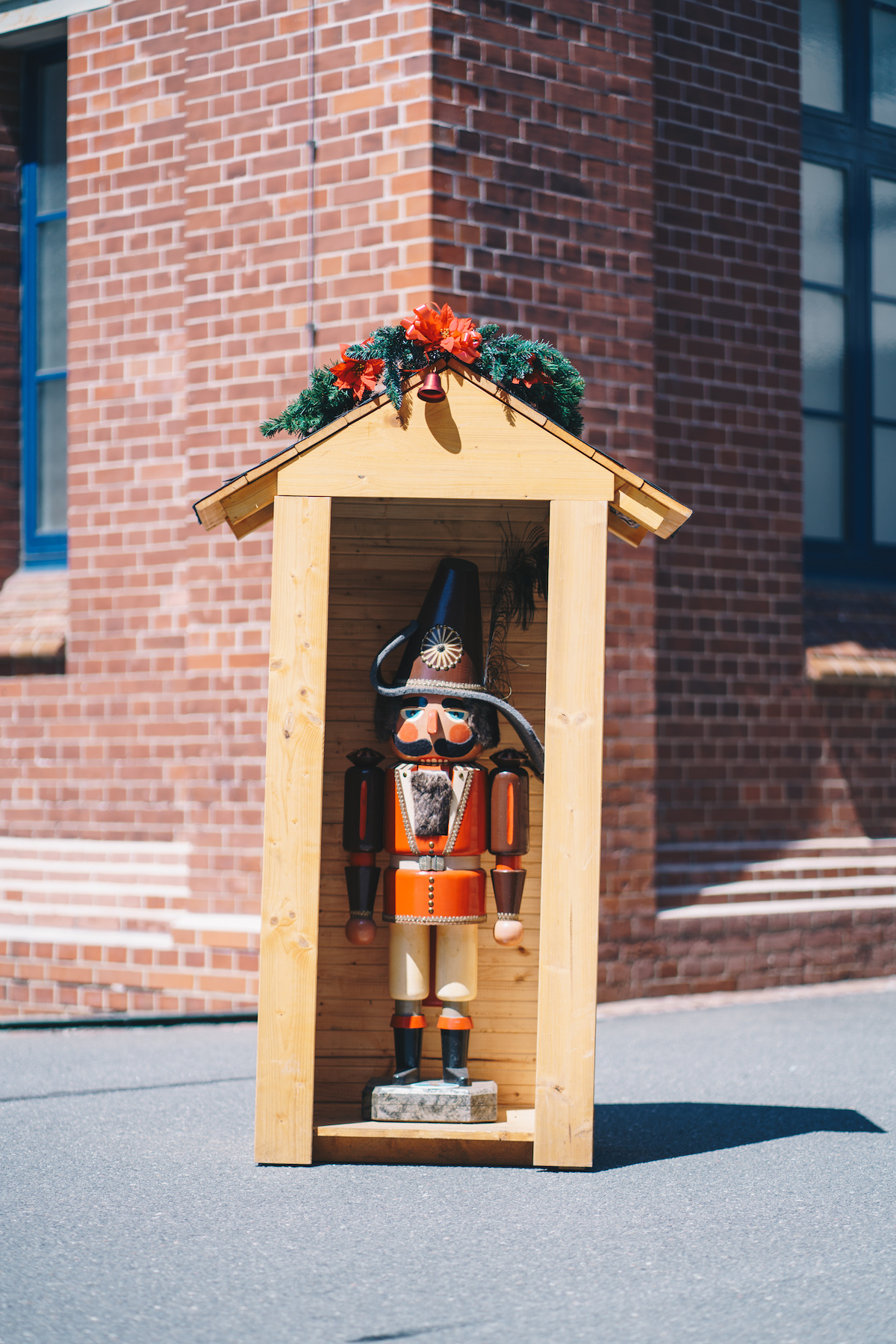 Ein sehr großer Nussknacker (Großfigur aus dem Erzgebirge) steht in einem mit Weihnachtsdekoration geschmückten kleinen Holzhaus.